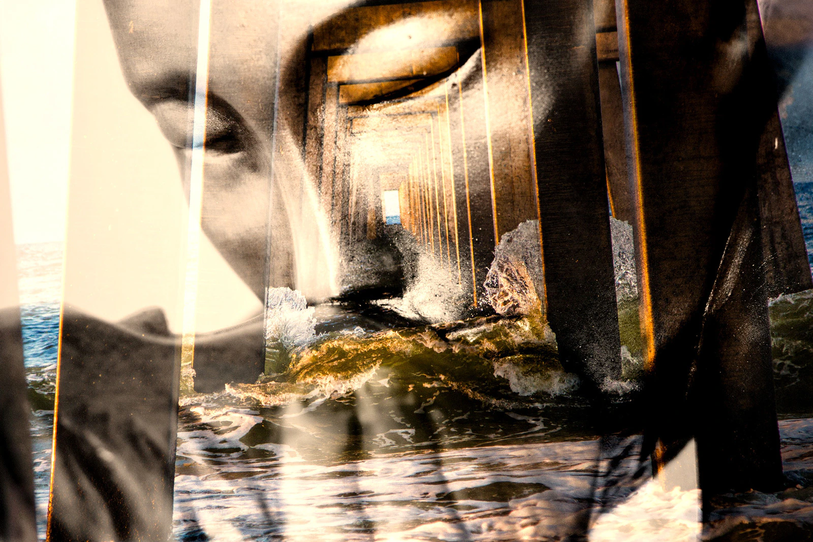 Digital collage: a woman's face in double exposure over surf breaking through the pilings of a wooden pier, in gold and deep blue